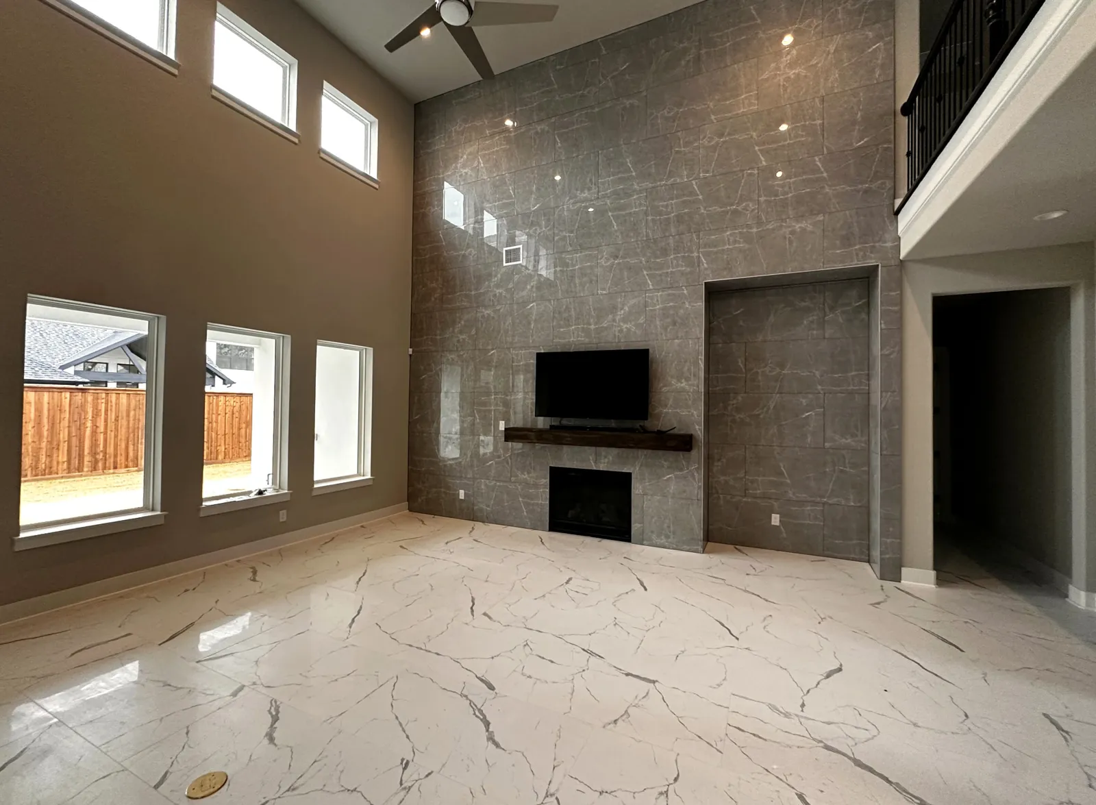 Two-story Dallas great room with polished marble-look tile flooring carried up into a floor-to-ceiling tile fireplace feature wall